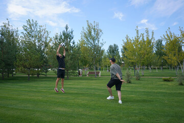 Fototapeta premium Two young adults engage in a lively game of volleyball outdoors in a sunny park, with vibrant greenery and a clear blue sky enhancing the cheerful atmosphere