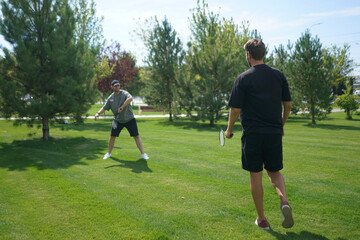 Obraz premium Two individuals engage in a friendly badminton match on a lush green lawn, surrounded by trees under a clear blue sky on a beautiful summer day