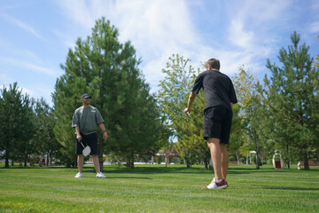 Obraz premium In a lush park, two friends play badminton on a beautiful sunny day. The vibrant greenery and clear sky create a perfect backdrop for their friendly match