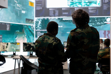 Fototapeta premium Diverse team of military personnel analyzing battlefield real time data on CCTV radar satellite system, transmitting information to soldiers in the field. Army superiors work on defense program.