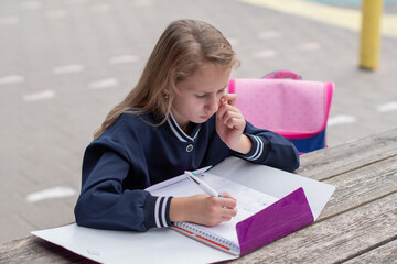 Teenage girl focused on solving complex math equation at wooden table in park outdoors, education...