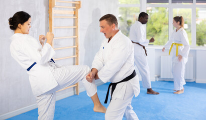 Sportive middle-aged man trainee of karate courses applying attack methods on his partner