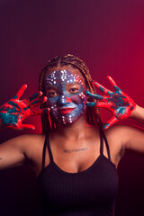 Woman with face painted with colorful paint and braids in her hair making gestures with her hands and fingers.