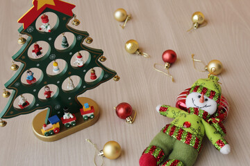 Stuffed snowman and Christmas tree toy on wood background for december holiday celebration. Xmas baubles, decoration for winter season in red and gold colors.