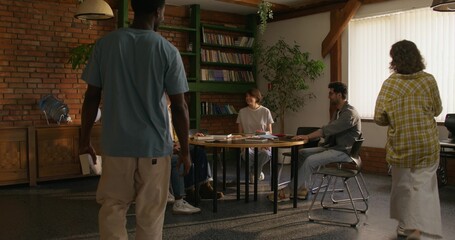 Young people of different nationalities gather at a table to study the Bible together. Stylish room, daylight