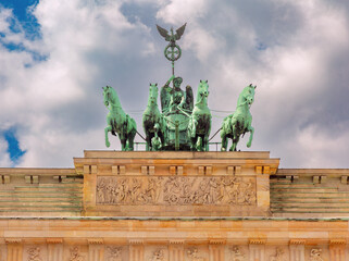 Obraz premium Close-up of the Quadriga sculpture atop the Brandenburg Gate in Berlin, Germany, featuring a four-horse chariot and the goddess of victory against a cloudy sky