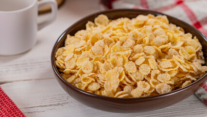 Bowl of crunchy corn flakes on wooden table. A bowl of crunchy corn flakes on a wooden table, perfect for breakfast or food-related projects.