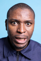 Fototapeta premium Portrait of security guard acting silly with funny faces on camera, pretending to be scared and fooling around against blue background. Playful agent feeling confident in uniform. Close up.