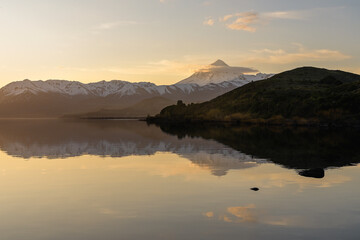 Snow covered volcano hiding behind mountains by the lake on a stunning golden sunrise