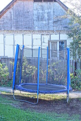 one big blue black empty trampoline stands on the ground in green grass on a summer street in a private yard