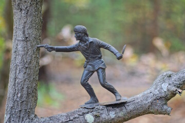 one big old dirty brown toy soldier stands on a tree branch in a summer park