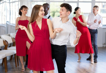 Obraz premium Positive couple, attractive long-haired woman in red dress and confident Hispanic guy, snapping fingers while rehearsing twist in dance studio ..