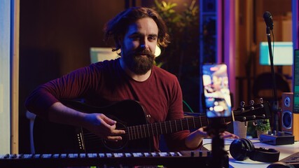 Guitarist instructor teaching guitar lessons online on internet, recording video on smartphone as a tutorial. Singer explaining acoustic instrument techniques, gives musical assistance. Camera A.