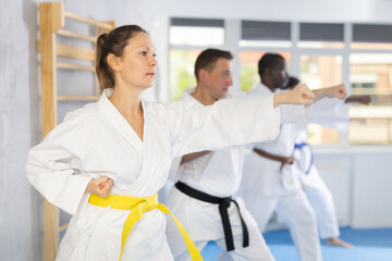 Obraz premium Diligent middle-aged woman attendee of karate classes practicing kata standing in row with others in sports hall