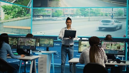 Indian manager supervising his employees team in observation room, people monitoring traffic through satellite system CCTV cameras. Diverse group working on surveillance tracking. Camera B.