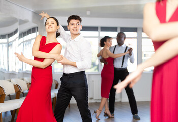 Fototapeta premium Happy young man and woman in elegant clothes performing ballroom dance in modern dancing room during celebration or party