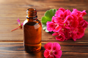 Geranium essential oil in bottle and beautiful flowers on wooden table