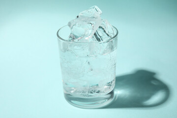 Refreshing water with ice in glass on turquoise background, closeup