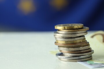 Stack of coins and euro banknotes on white table, closeup. Space for text