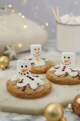 Delicious cookies with snowmen made of marshmallows on white table, closeup