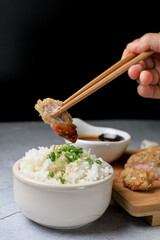 Hand use chopstick eating Japanese tonkatsu fried pork cutlet recipe with sweet sour sauce and rice on wooden broad. Asian food.
