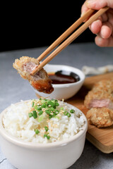 Hand use chopstick eating Japanese tonkatsu fried pork cutlet recipe with sweet sour sauce and rice on wooden broad. Asian food.