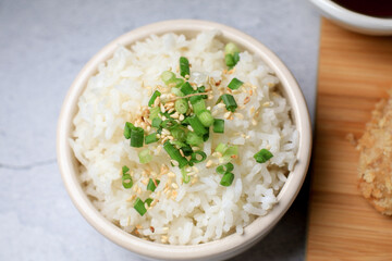 Steamed rice with black sesame seeds and spring onion in ceramic bowl on table. Japanese and Asia eat with food