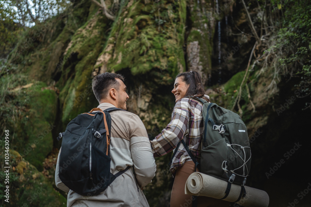 Wall mural back view of hiker couple in front cave in the forest