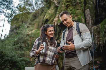 hiker couple backpackers stand in front waterfall and use cellphone