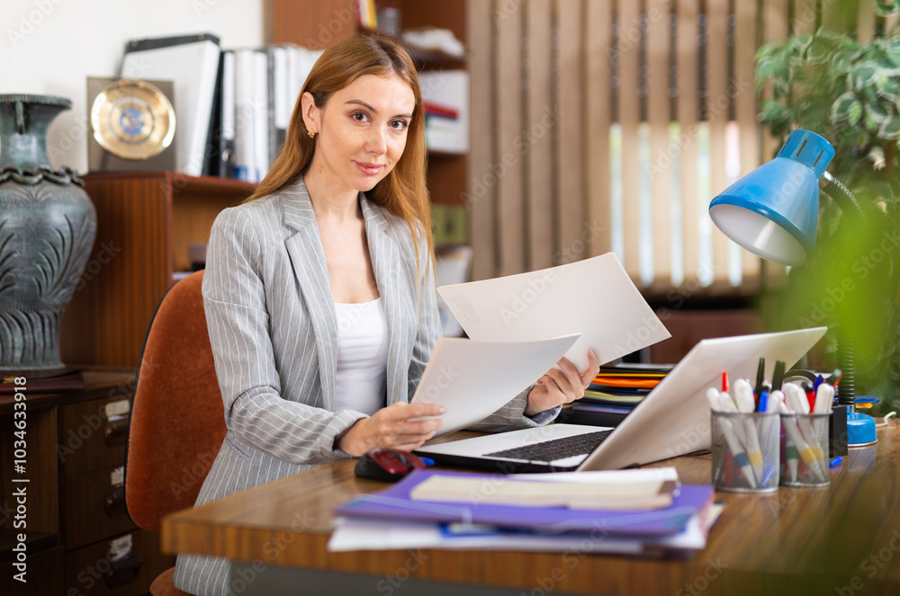 Wall mural European female secretary sitting at desk and doing her daily paperwork.