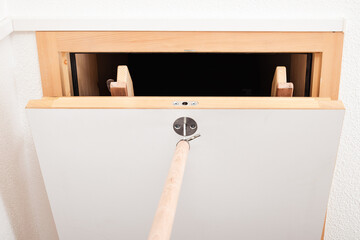 Attic hatch or loft door is opened with handle. Wooden extension pole used to pull down loft sliding ladder with hatch or attic door. Used to access a loft, storage space or attic. Selective focus.