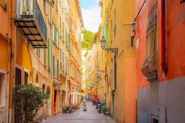 Fototapeta premium A tourist pulls her suitcase along a narrow alley in the colorful Vieux Nice Old town of Nice, France, on the French Riviera, Cote d'Azur of the Mediterranean Sea.