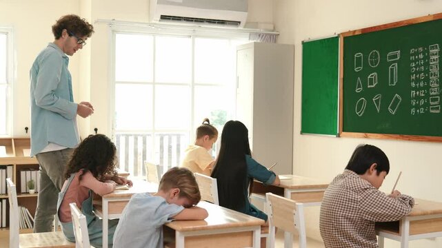 Skilled teacher walking at classroom while looking at student homework. Professional instructor checking smart children notebook while student doing test or working on homework at classroom. Pedagogy.