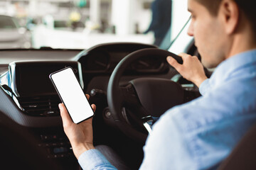Smart Driving App. Man Using Smartphone Sitting In New Car Buying Vehicle In Auto Center. Selective...