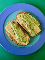 Toasted sourdough ciabatta bread with slices of Swiss cheese and guacamole on a plate.