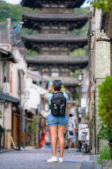 Unrecognizable young Latina woman, dressed casually with a backpack and smartphone, explores the streets near Hōkan-ji Pagoda in Kyoto, Japan, enjoying the sights and taking pictures.