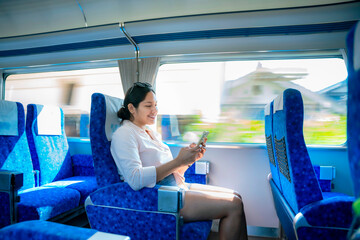 A happy young Latina woman, seated comfortably on a high-speed train in Japan, smiles while using...