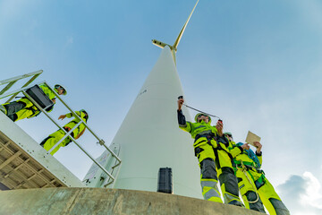 A team of engineers inspects and maintains a large wind turbine at a renewable energy wind farm. Green technology and sustainable practices are at the forefront of renewable energy development. © ultramansk