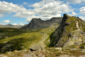 A narrow path going along the top of the mountain to a high pass along the mountain in the form of a lying man on a sunny summer day.