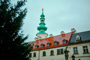 Photograph of a historic building in Bratislava, Slovakia, showcasing a distinctive green tower with a clock and red-tiled roof.