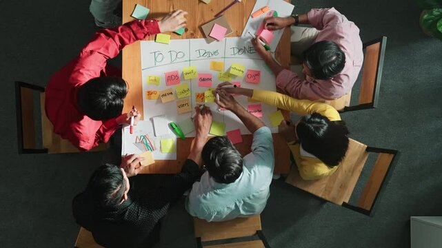 Top view of people writing and making scrum task board while writing marketing and planning strategy at colorful sticky notes. Smart team manage work performance by using kanaban board. Convocation.