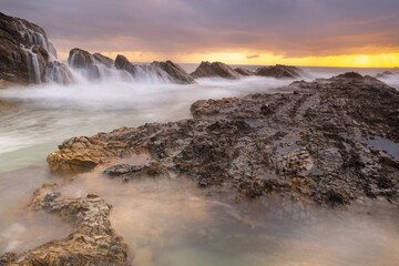Dramatic scene of  ocean waves crashing over large  jagged coastal sea rocks