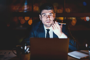 Businessman Using Voice Assistant On Mobile Phone Sitting At Laptop In Modern Office At Night. Selective Focus