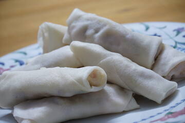 Heap of raw spring rolls(lumpia) on the plate. Frozen food on wooden tables.