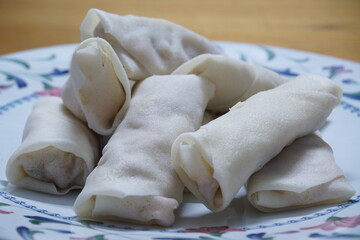 Heap of raw spring rolls(lumpia) on the plate. Frozen food on wooden tables.