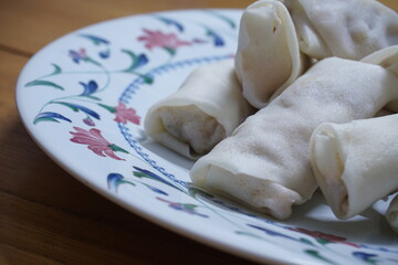 Heap of raw spring rolls(lumpia) on the plate. Frozen food on wooden tables.