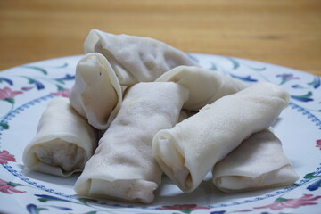 Heap of raw spring rolls(lumpia) on the plate. Frozen food on wooden tables.