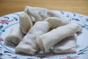 Heap of raw spring rolls(lumpia) on the plate. Frozen food on wooden tables.