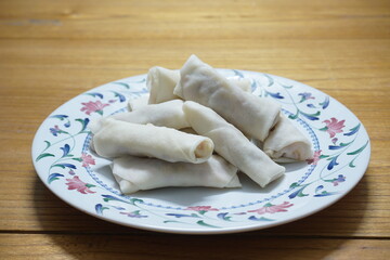 Heap of raw spring rolls(lumpia) on the plate. Frozen food on wooden tables.