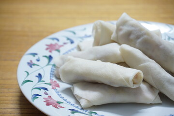 Heap of raw spring rolls(lumpia) on the plate. Frozen food on wooden tables.